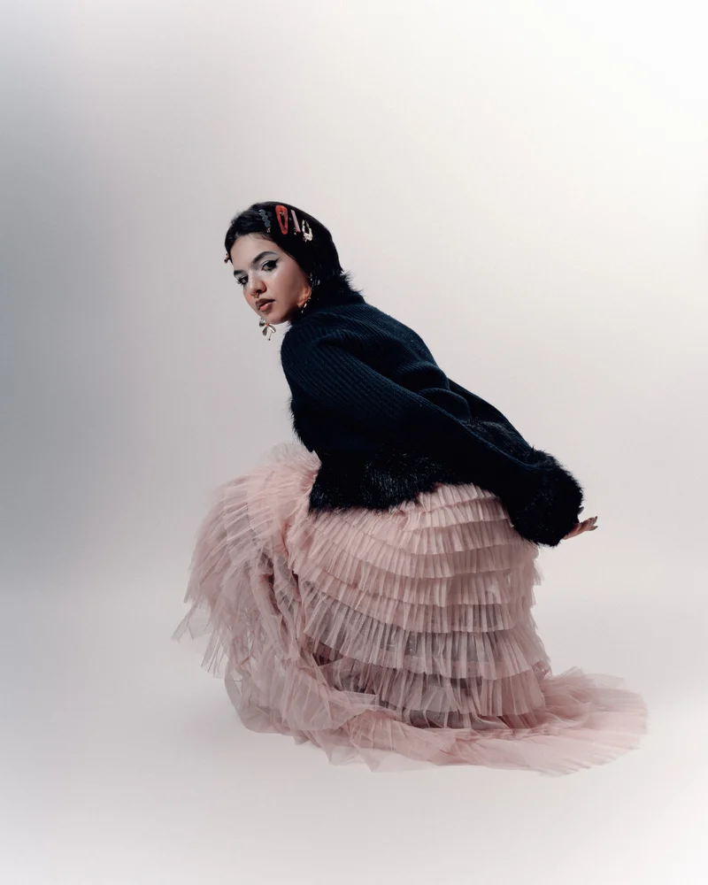 Alanis em um ensaio criativo, com casaco preto e saia rosa de tule.